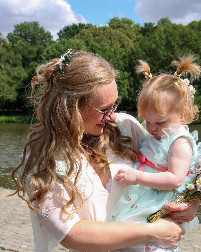 The bride and the little flower girl sharing a bouquet moment by the lake